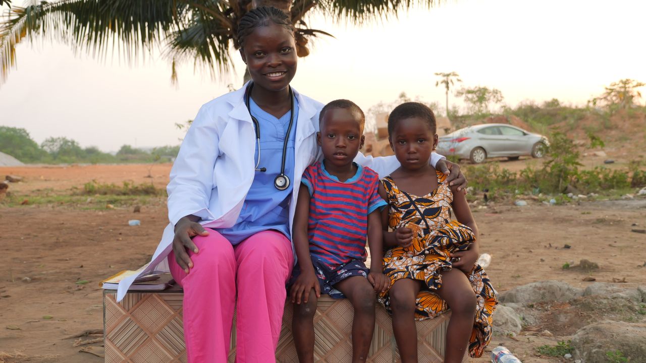 Female healthcare worker smiles with two children outside, showcasing community care.